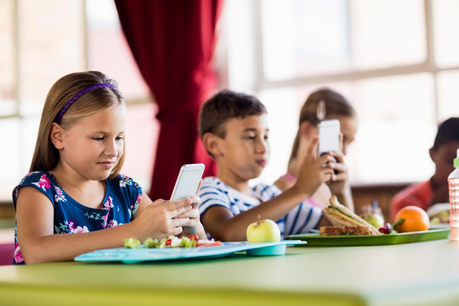 Kinder mit Smartphone und Essen in der Schule