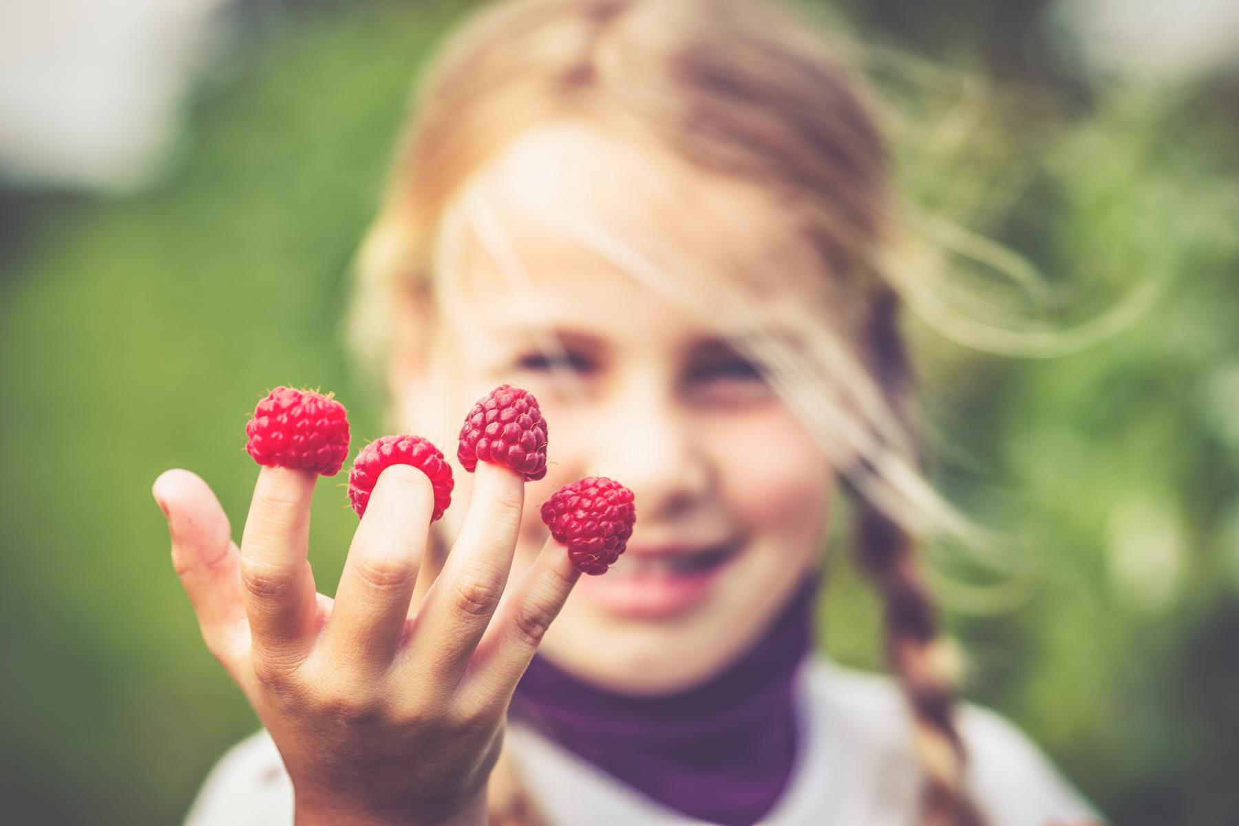 Mädchen mit Himbeeren auf den Fingerspitzen